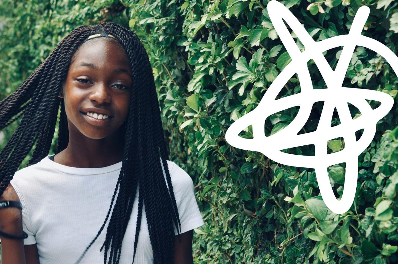 A young girl with long braided hair smiles at the camera while standing against a lush green wall of leaves. She wears a plain white T-shirt and has a confident expression. To the right, there is a large, white abstract graphic resembling a tangled line drawing, overlapping the greenery. The overall atmosphere is vibrant and cheerful.