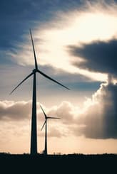 wind turbines shown on a field with the sun behind clouds