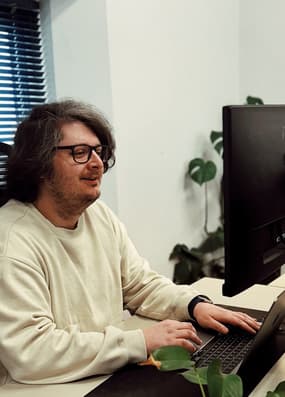 A male web developer working on a laptop with a large monitor in front of him