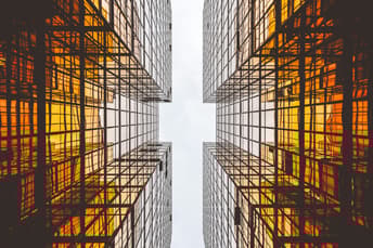 A photo looking up between two buildings made up of glass, which are white and amber coloured