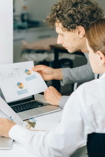 A man and a woman are at a laptop on a desk analysing analytics from a website relating to carbon