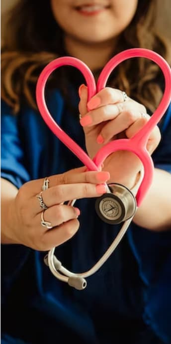 A woman wearing a navy blue outfit is holding out a stethoscope that has been manipulated to be in the shape of a heart