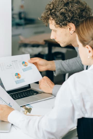 A man and a woman are at a laptop on a desk analysing analytics from a website relating to carbon