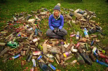 A woman sits on the grass surrounded by a huge array of plastic items she has collected from the sea. She looks shocked and sad.