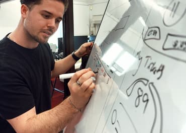 Person drawing UX features for a dashboard on a whiteboard - he is considering intently what he is writing. Wordpress website design agency