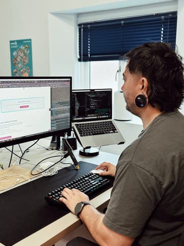 Male web developer working on a website using a large computer monitor and laptop