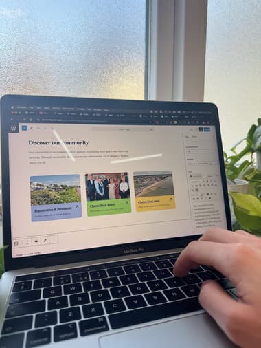 Wordpress CMS editor for a website that has the heading 'Discover our community' on the page. A person's hand is at the laptop, typing.