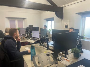 A group of four desks with three men and a woman sitting at them all looking thoughtfully at their computer screens.