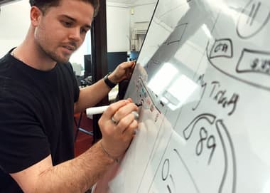 Person drawing UX features for a dashboard on a whiteboard - he is considering intently what he is writing. Wordpress website design agency​