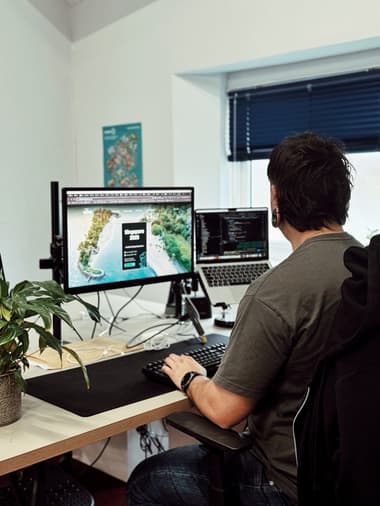 Male developer working on a website with two screens in front of him, one of which is a laptop
