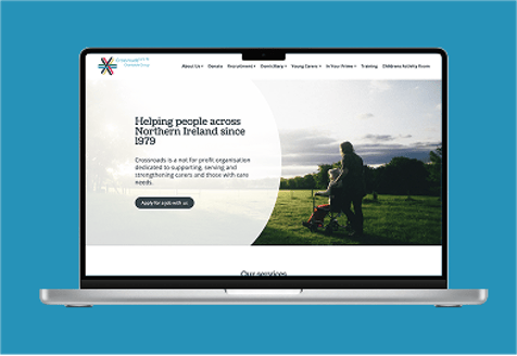 A blue background with a laptop showing a website for Crossroads Care Northern Ireland.