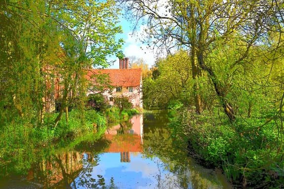 Coggeshall Abbey sitting next to water, with lots of lush green trees on each side.