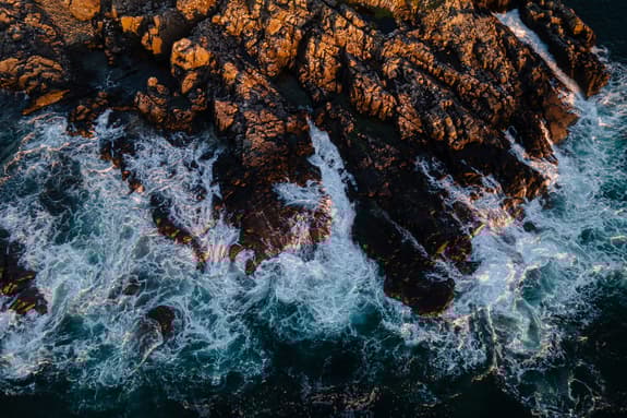 A birds eye view of waves crashing against a rocky coastline