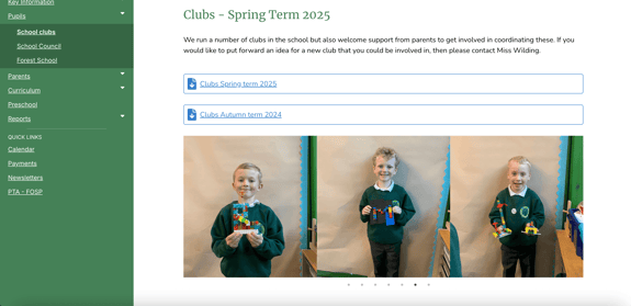 Three children are standing side by side in a classroom. The child on the left, wearing a green sweater, is holding a colourful model made of building blocks. The child on the right, also in a green sweater, is smiling and holding two different models. The child in the middle is also holding two models. The background features plain beige paper and green walls.
