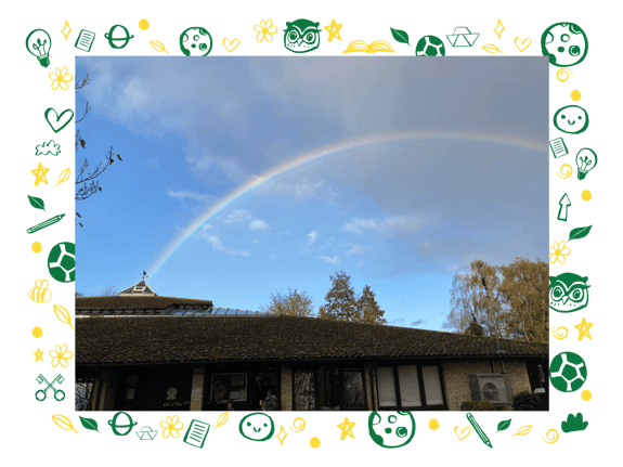 A rainbow arches across a partly cloudy sky above a building with a sloped roof, featuring a glass section. The structure has large windows and displays various items in front of it. Surrounding the building are trees with autumn foliage. The image is framed by a decorative border filled with colourful icons, including light bulbs, books, flowers, and sports equipment.