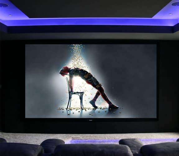 A home cinema screen showing the tops of comfy looking chairs at the bottom, purple lights on the ceiling and a screen depicting a scene from a film