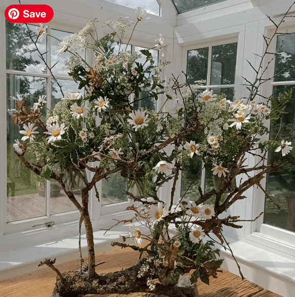 A centrepiece display of flowers and foliage displayed inside a conservatory with the light beaming in