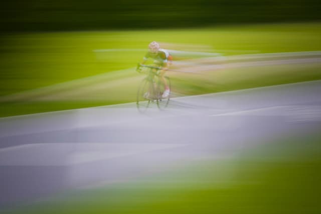 A photo of a cyclist on a track surrounded by green on each side, in a blurred style