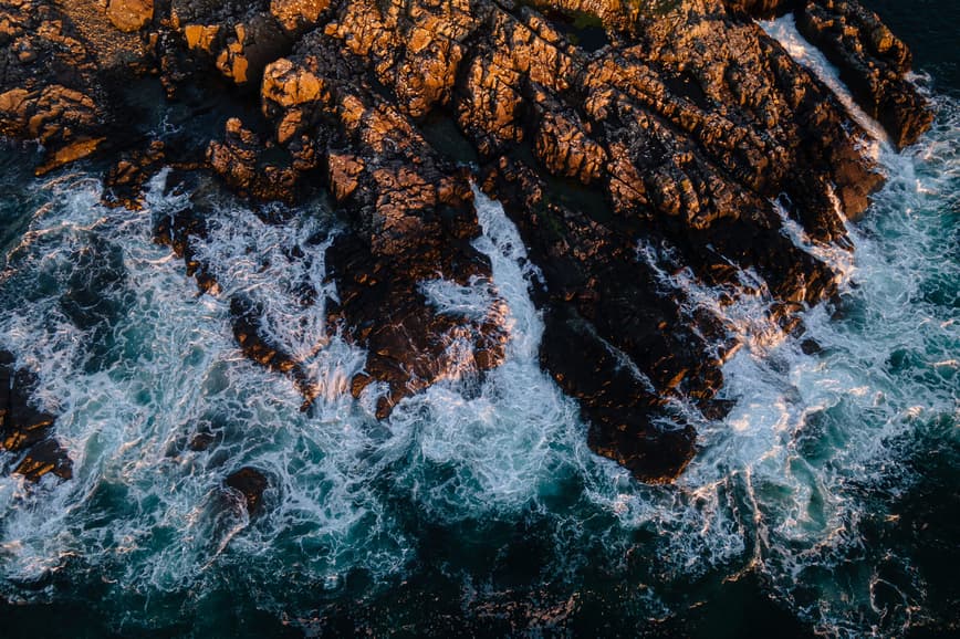 A birds eye view of waves crashing against a rocky coastline
