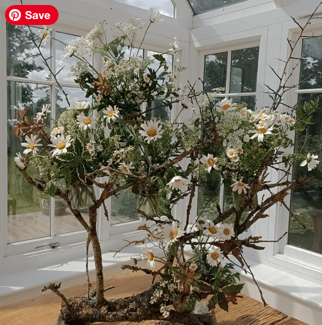A centrepiece display of flowers and foliage displayed inside a conservatory with the light beaming in