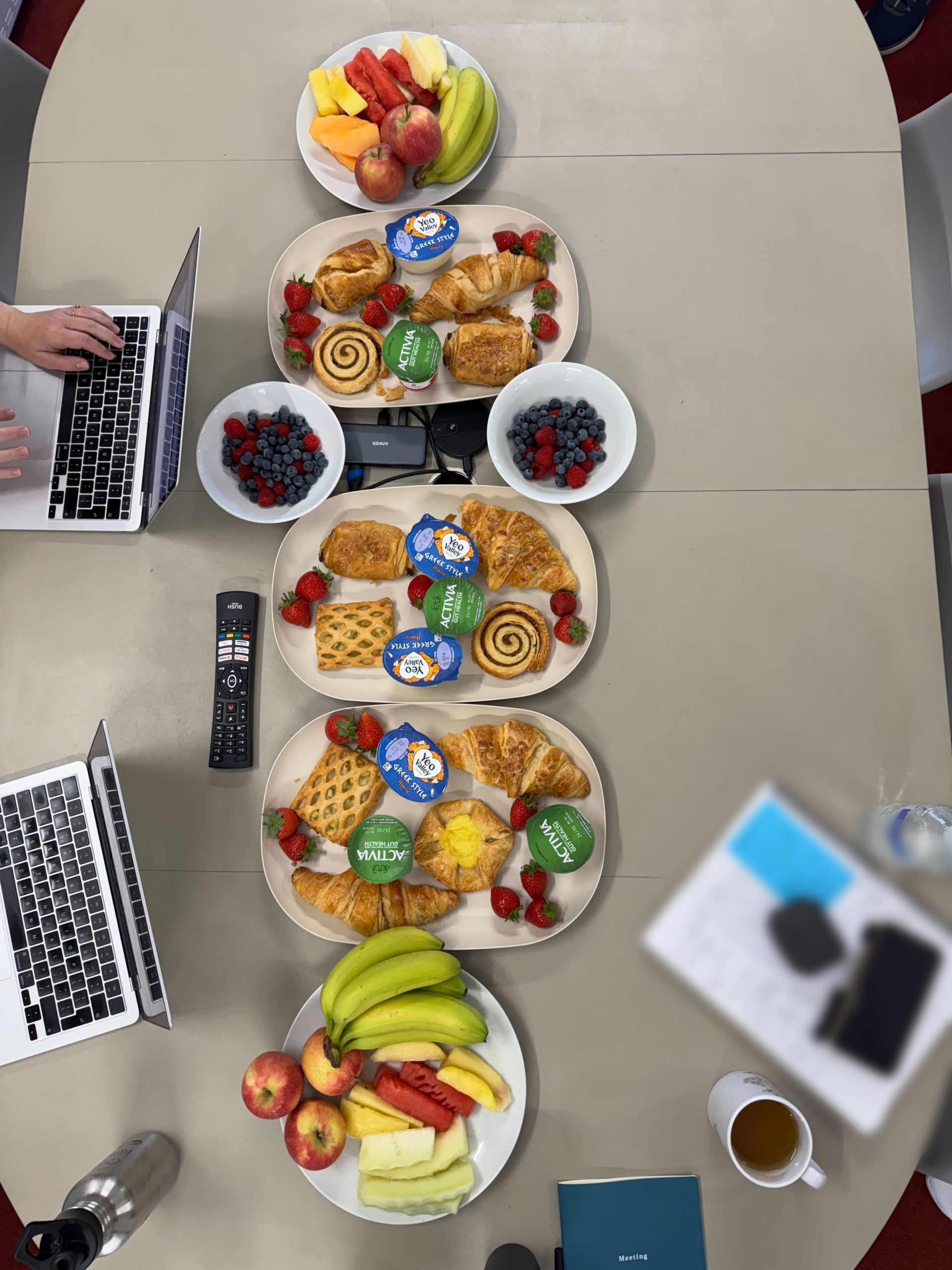 Plates of breakfast food laid out on a table with laptops dotted around and a writing pad